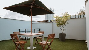 Una terraza en la azotea con una mesa, sillas, una sombrilla grande y una planta en maceta.