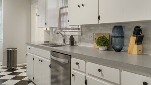 Cocina moderna con armarios blancos, lavavajillas de acero inoxidable, un lavabo y una encimera con una planta en maceta y un bloque de cuchillos.