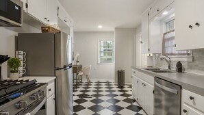 Una cocina moderna con suelo a cuadros blanco y negro, electrodomésticos de acero inoxidable y armarios blancos.