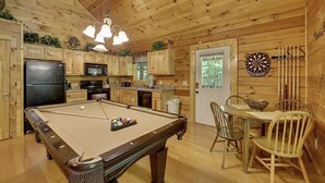 A wooden cabin interior with a pool table, dining area, kitchen, and dartboard. - Creekside Paradise Found! One-Bedroom Mountain Cabin in Pigeon Forge (Sevierville)