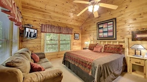 A cozy wooden cabin bedroom with a bed, a couch, a ceiling fan, and a window with a view of the outdoors. - Creekside Paradise Found! One-Bedroom Mountain Cabin in Pigeon Forge (Sevierville)