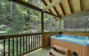 Une terrasse en bois dotée d’un jacuzzi et d’un espace salon, le tout entouré d’un paysage boisé.