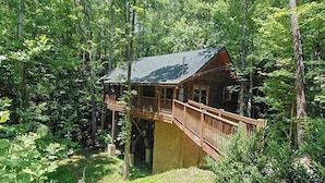 A cabin with a wooden deck and a staircase leading to a balcony, surrounded by dense forest. - Creekside Paradise Found! One-Bedroom Mountain Cabin in Pigeon Forge (Sevierville)
