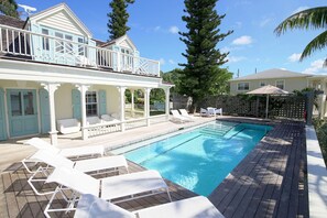A pool area with lounge chairs, a wooden deck, and a building with a balcony. - Harbourside house with private pool - amazing sea views! (Governor's Harbour)