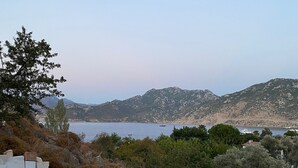 A rectangular swimming pool with a clear blue water surface, surrounded by stone steps and a metal handrail. In the background, there is a view of a body of water and distant mountains. - Mavi Melek Hotel (Marmaris)