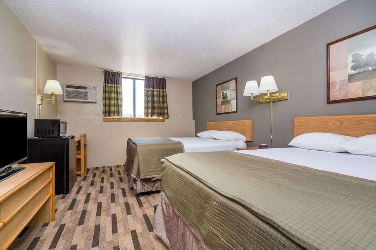 A hotel room with two beds, a desk, a television, and a window with curtains.