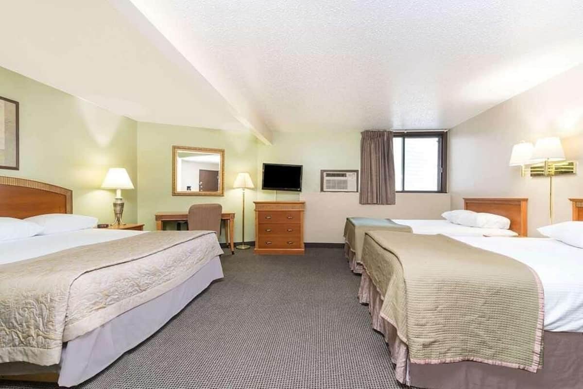 A hotel room with two beds, a desk, a chair, a television, and a window with curtains.