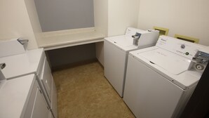 A laundry room with two white washing machines, a countertop, and a window. - Bison Inn and Suites (Fargo)