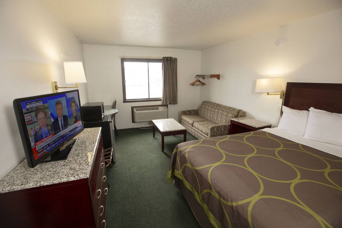 A hotel room with a bed, a television, a sofa, a desk, and a window with curtains.