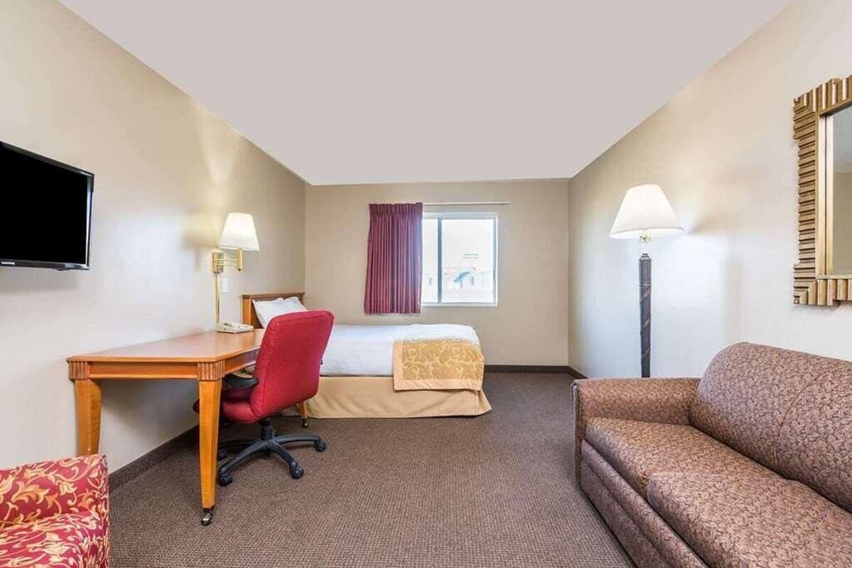 A hotel room with a bed, a desk with a chair, a sofa, a TV mounted on the wall, and two lamps.