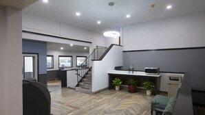 A modern hotel lobby with a herringbone floor pattern, a staircase, a reception desk, and seating area. - Bison Inn and Suites (Fargo)
