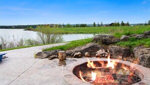 A fire pit with a lake view, surrounded by rocks and greenery.