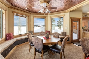 A cozy dining area with a wooden table and chairs, large windows with snowy views, and a ceiling fan.