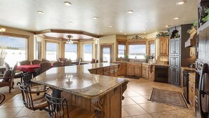 A spacious kitchen with a large island, wooden cabinets, and a view of a snowy landscape through large windows.