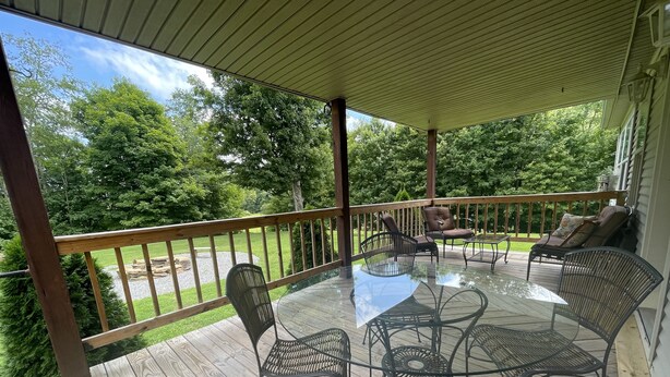 A covered outdoor deck with a glass-top table and metal chairs, surrounded by a wooden railing.