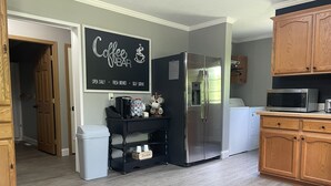 A kitchen with a stainless steel refrigerator, a To-Go cooler, a coffee bar sign, and wooden cabinets.