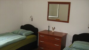 Een kleine, eenvoudige kamer met twee eenpersoonsbedden, een houten dressoir en een spiegel aan de muur.