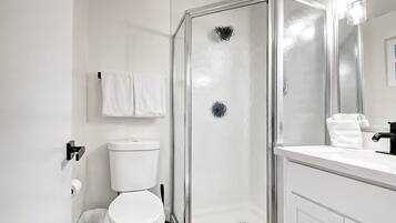 Un baño moderno con cabina de ducha de vidrio, inodoro y lavabo con espejo.