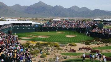 Un campo de golf con espectadores, carpas y montañas al fondo.
