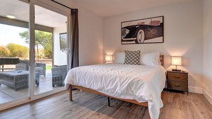 A bedroom with a bed, a nightstand, a lamp, a painting, and a sliding glass door leading to an outdoor area.