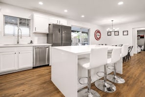 A modern kitchen with white cabinetry, stainless steel appliances, and a central island with bar stools.