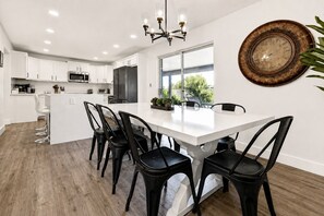 A modern kitchen with white cabinets, a central island with bar stools, a dining table with chairs, and a decorative wall clock. - Scottsdalestays The Amazing 6BR-3BA on Acre-Resort Pool-Grass and Sport Courts (Scottsdale)
