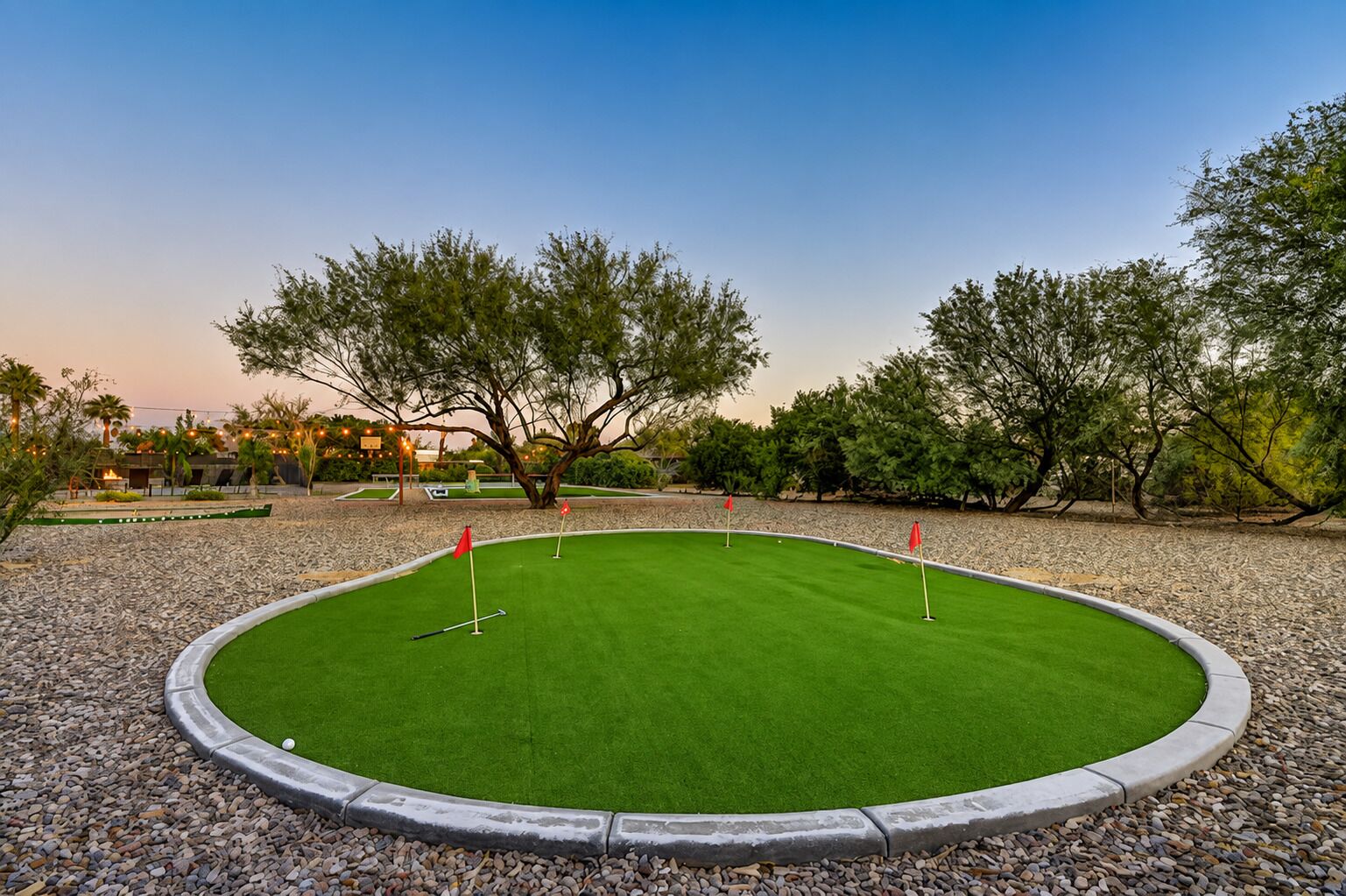 A well-maintained golf course with a putting green, surrounded by trees and a gravel border.