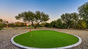 A well-maintained golf course with a putting green, surrounded by trees and a gravel border.