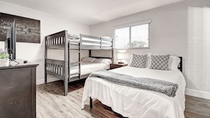 A bedroom with a bunk bed, a single bed, a desk with a computer, and a window with blinds.