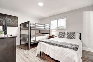 A bedroom with a bunk bed, a single bed, a desk with a computer, and a window with blinds.