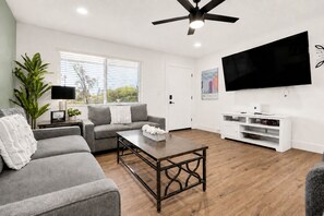 A living room with a grey sofa, a coffee table, a TV, and a white entertainment unit. - Scottsdalestays The Amazing 6BR-3BA on Acre-Resort Pool-Grass and Sport Courts (Scottsdale)