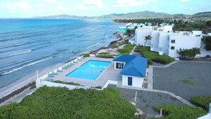 A coastal hotel with a swimming pool, beachfront view, and white buildings.