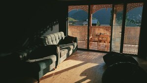 En stue med en sofa og en puf, trægulv og en stor skydedør til et udendørs område med et mønstret hegn.