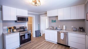 A modern kitchen with white cabinets, stainless steel appliances, and a wooden floor.