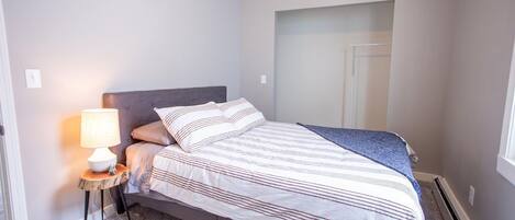 A neatly made bed with striped bedding, a bedside lamp, and a small wooden side table.