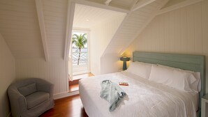 Ein Schlafzimmer mit einem Bett, einem Nachttisch, einer Lampe, einem Sessel und Blick ins Freie durch ein Fenster.