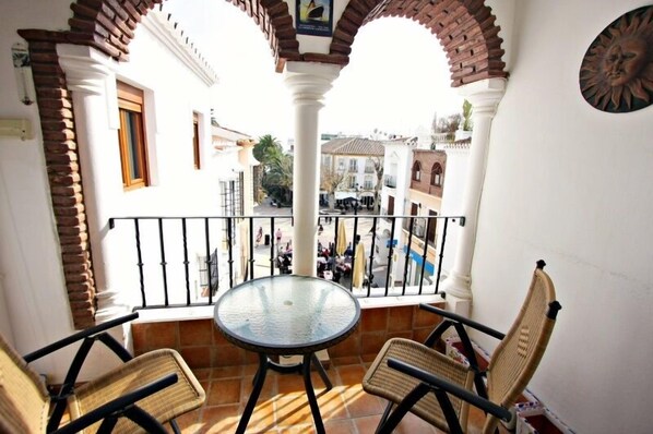 Enjoy the view from this balcony with a glass table and two chairs, surrounded by white columns with brick accents.