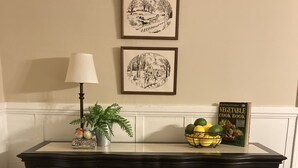 A dark wooden cabinet with four drawers, a small potted plant, a welcome sign, and a book titled "Vegetable Cook Book" on top.