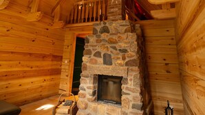A log cabin interior with a stone fireplace, wooden beams, and a cozy seating area.