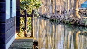 A wooden dock extending into a calm river, surrounded by trees and a building with a visible window and door.