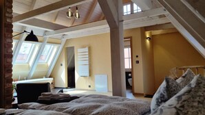 A bedroom with a sloped ceiling, skylight windows, a bed with a patterned blanket, a bedside table, and a hanging light fixture.