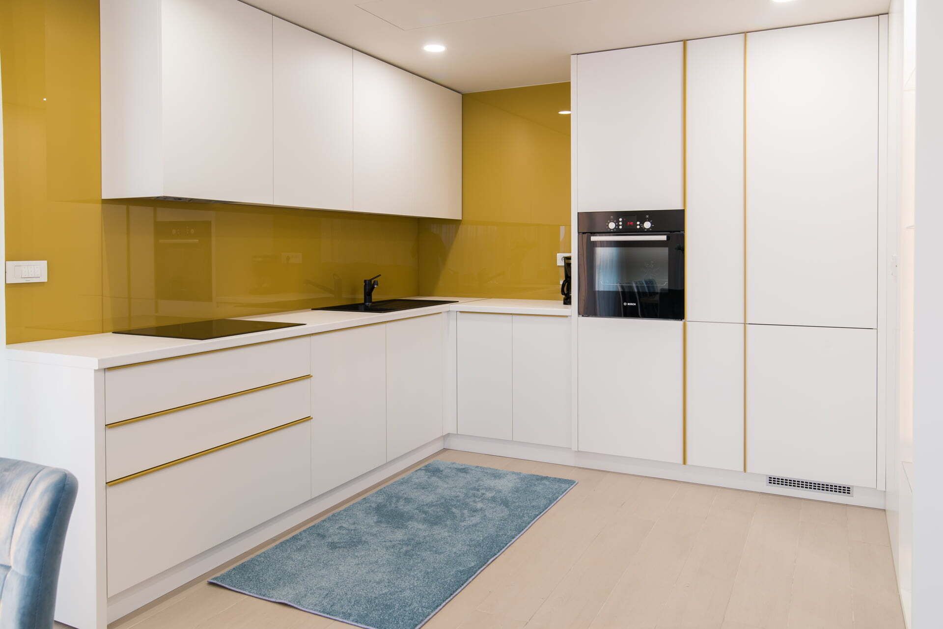 Una cucina compatta con mobili bianchi, un forno nero e una parete gialla a contrasto.
