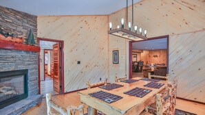 Ein rustikaler Essbereich aus Holz mit einem großen Tisch, Stühlen, einem Steinkamin und einer Holzbalkendecke.