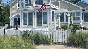 A two-story house with a white picket fence, a balcony, and an American flag. - BEAUTIFUL LAKE MICHIGAN BEACH HOUSE just a 5-minute walk to the water’s edge! (Muskegon)