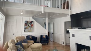 A spacious living area with a high ceiling, a white fireplace, and a staircase leading to an upper level. - BEAUTIFUL LAKE MICHIGAN BEACH HOUSE just a 5-minute walk to the water’s edge! (Muskegon)