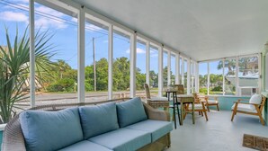 A sunroom with a blue sofa, wicker furniture, and large windows offering a view of the outdoors. - Pet Friendly Beach Cottage - Walk to the Beach Gated Access - Fenced in Yard - Bidawee (Panama City Beach)