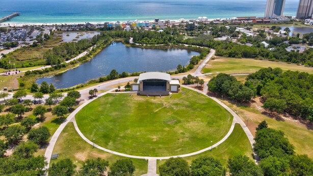 An aerial view of a park with a central stage, surrounded by a circular lawn, a lake, and a beach area. - Pet Friendly Beach Cottage - Walk to the Beach Gated Access - Fenced in Yard - Bidawee (Panama City Beach)