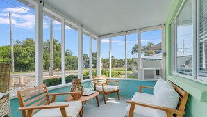 A covered porch with wooden chairs and a table, large windows offering a view of the outdoors. - Pet Friendly Beach Cottage - Walk to the Beach Gated Access - Fenced in Yard - Bidawee (Panama City Beach)