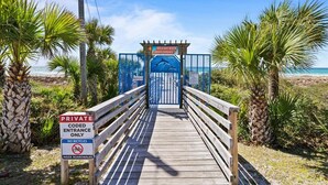 A private beach entrance with a wooden walkway, palm trees, and a sign indicating no bicycles allowed. - Pet Friendly Beach Cottage - Walk to the Beach Gated Access - Fenced in Yard - Bidawee (Panama City Beach)