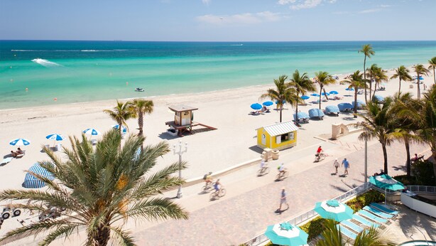 Une plage avec une eau turquoise et limpide, des palmiers et des parasols de plage.